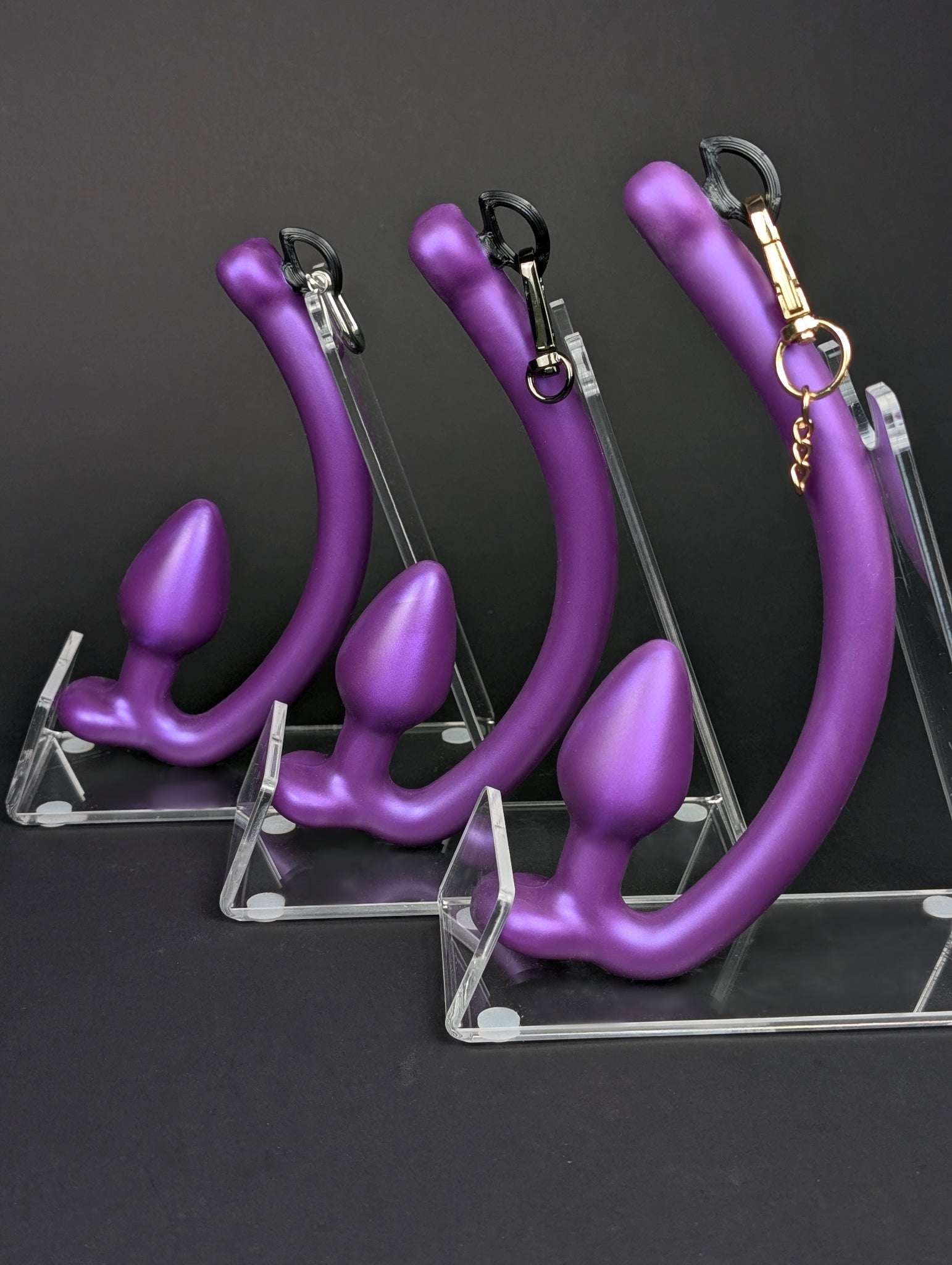 Purple silicone butt plugs for clip on tail hooks on clear stands against a black background