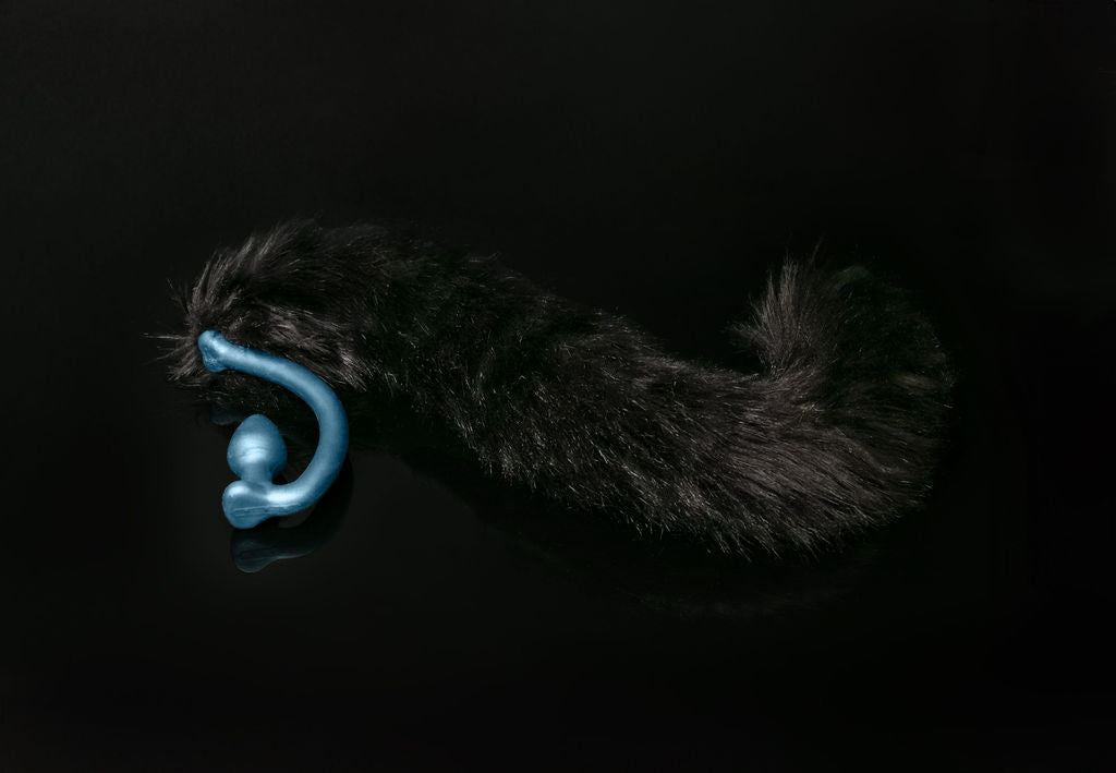 Long hair, black cat tail butt plug made of silicone and faux fur, but the plug is hooked so when worn, the tail sits at the bottom of the lumbar area. It’s laying flat on a black background.::Blue