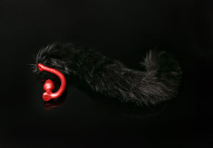 Long hair, black cat tail butt plug made of silicone and faux fur, but the plug is hooked so when worn, the tail sits at the bottom of the lumbar area. It’s laying flat on a black background.::Red