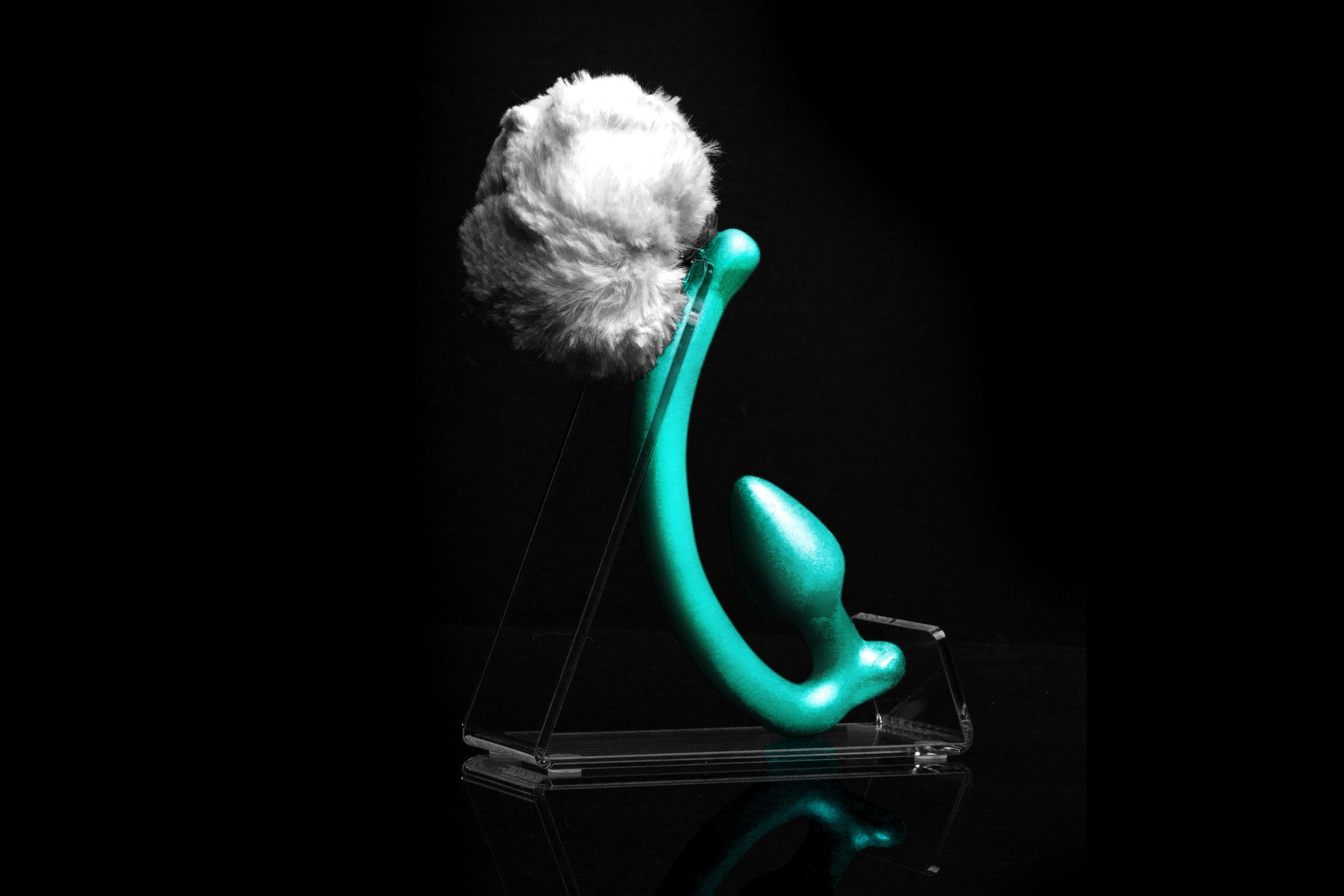 White Rabbit tail butt plug made of silicone and white faux fur, but the plug is hooked so when worn, the tail sits at the bottom of the lumbar area. It’s laying flat on a black background.::Mint