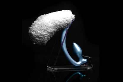 Sheep tail butt plug made of silicone and faux fur, but the plug is hooked so when worn, the tail sits at the bottom of the lumbar area. It’s laying flat on a black background.::Blue
